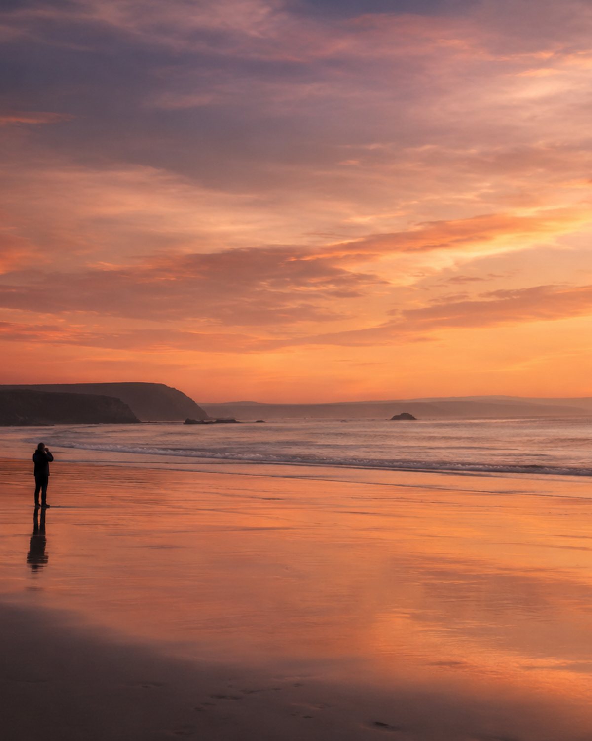 A solitary figure photographing the sea at sunset